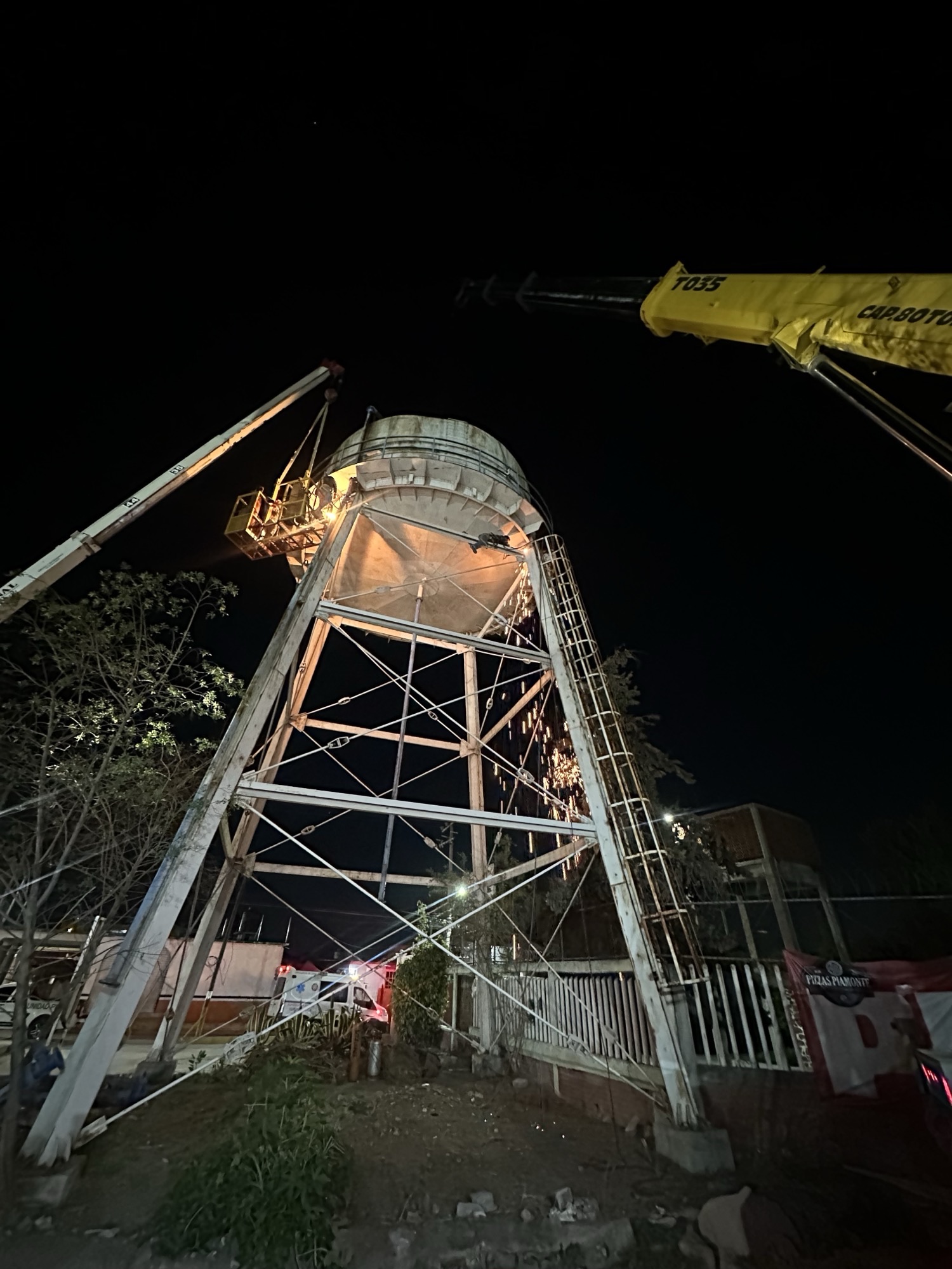 Acceso de personal en canastilla elevada por grúa telescópica hacia un punto de trabajo en altura de noche